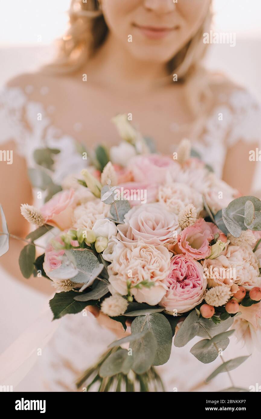 Primo piano di un bouquet di rose di pesche, garofani, eucalipto. La sposa in un abito bianco a maniche lunghe tiene un bouquet nelle mani. Foto Stock