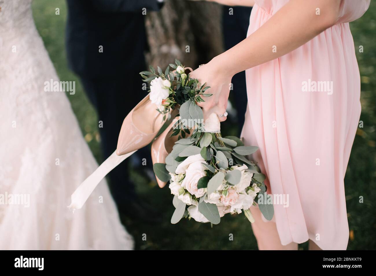 Primo piano di un bouquet di rose di pesche, garofani, eucalipto. La sposa in un abito bianco a maniche lunghe tiene un bouquet nelle mani. Foto Stock