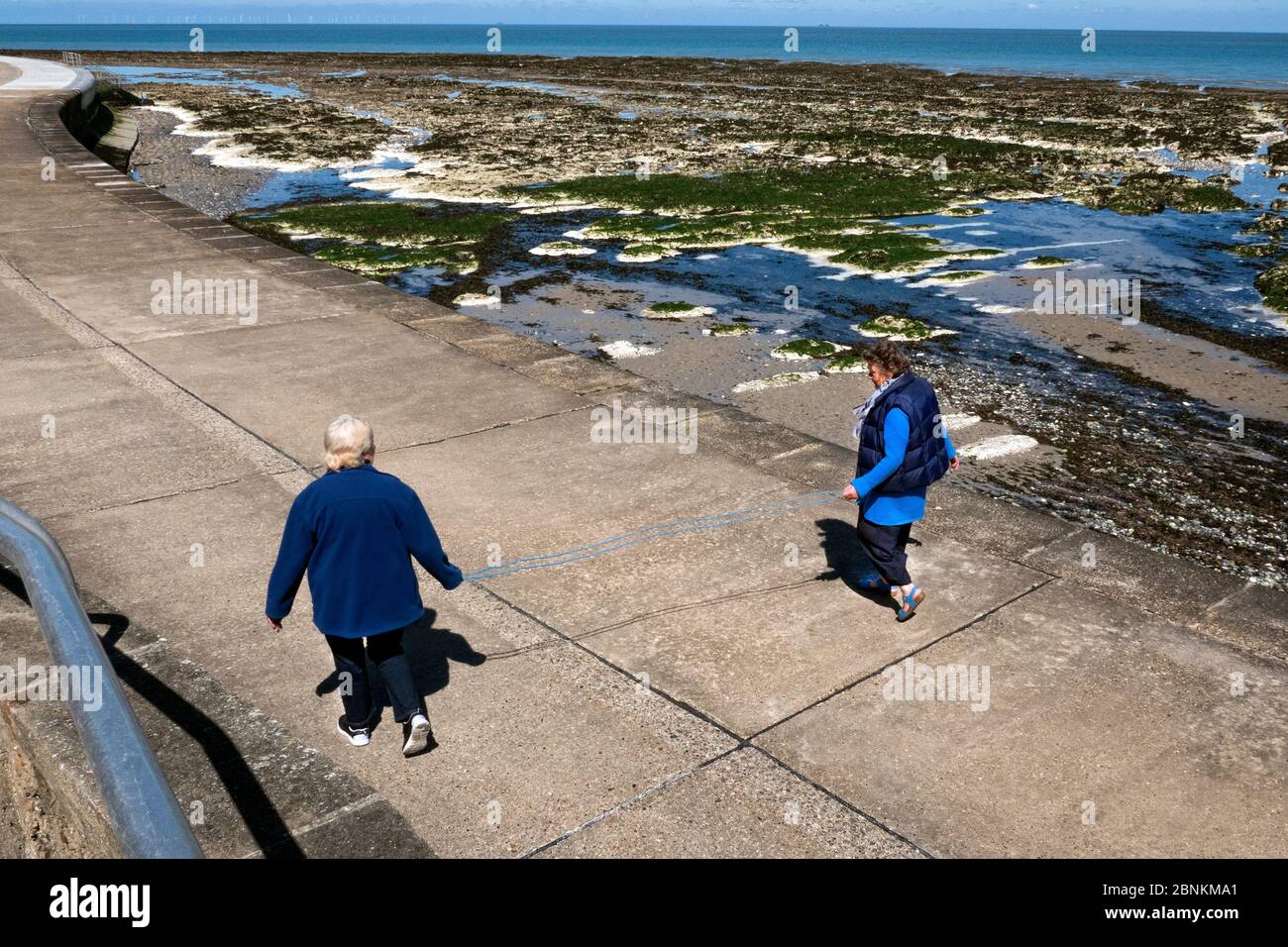 Due donne pensionati che usano una corda di 2 metri per la distanza sociale nel blocco corona-virus Foto Stock