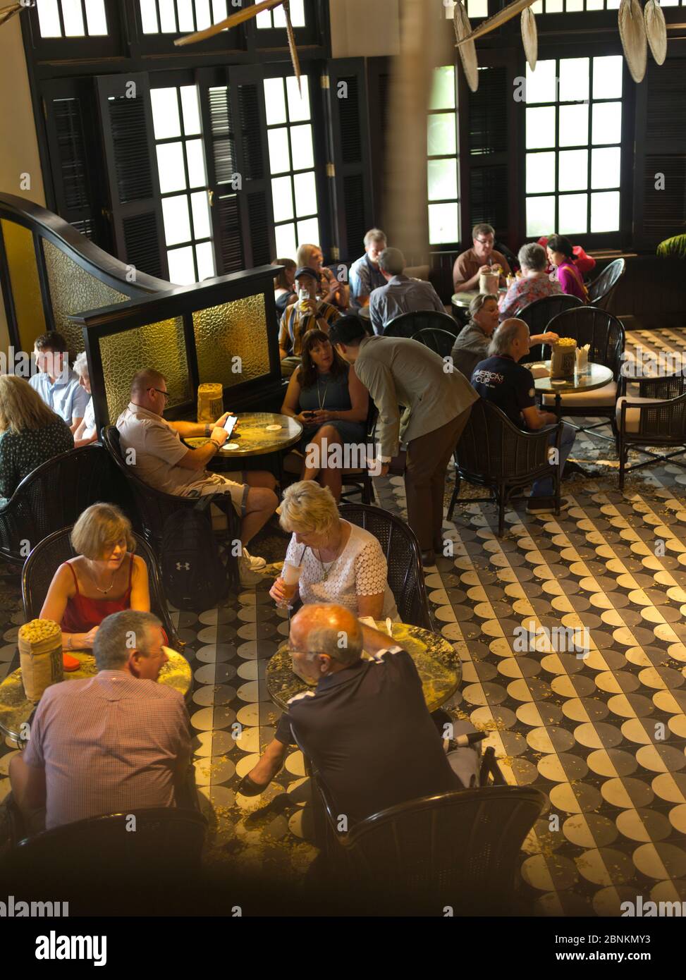 dh Long bar RAFFLES HOTEL SINGAPORE Tourist People relax with drinks at Tables hotels Colonial pub Foto Stock
