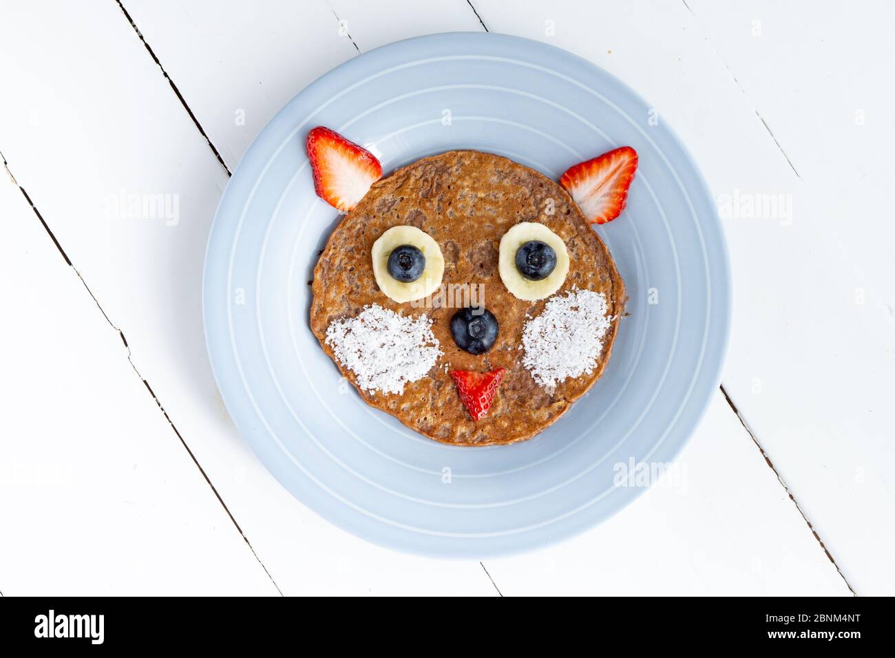 Pancake creativo con farinata d'avena per i bambini. Gatto o orso in una piastra isolata su sfondo bianco. Sana colazione vegetariana, pranzo o spuntino. Vista dall'alto, primo piano Foto Stock