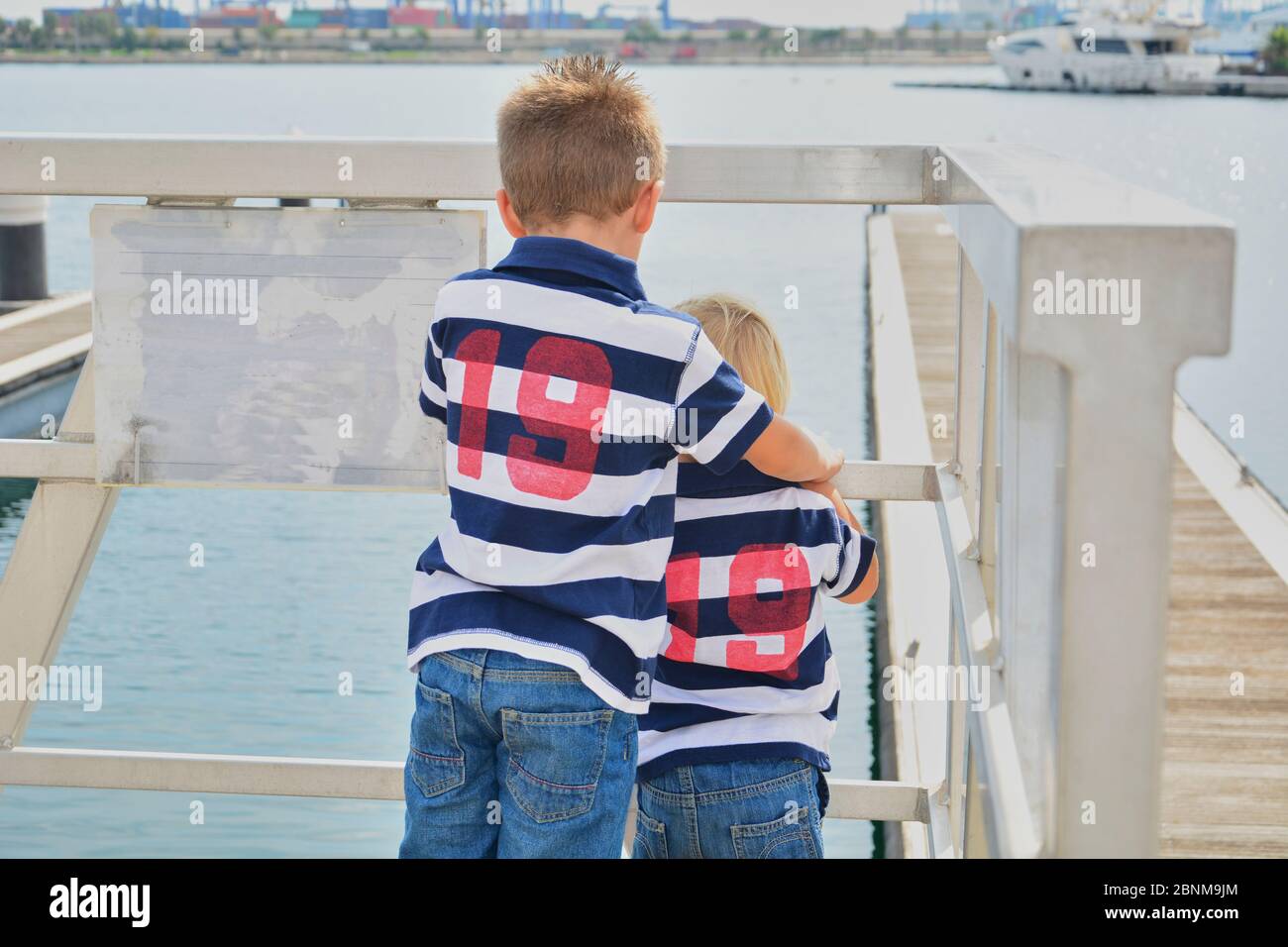 Due bambini che guardano attraverso una recinzione al mare, amicizia e amore Foto Stock