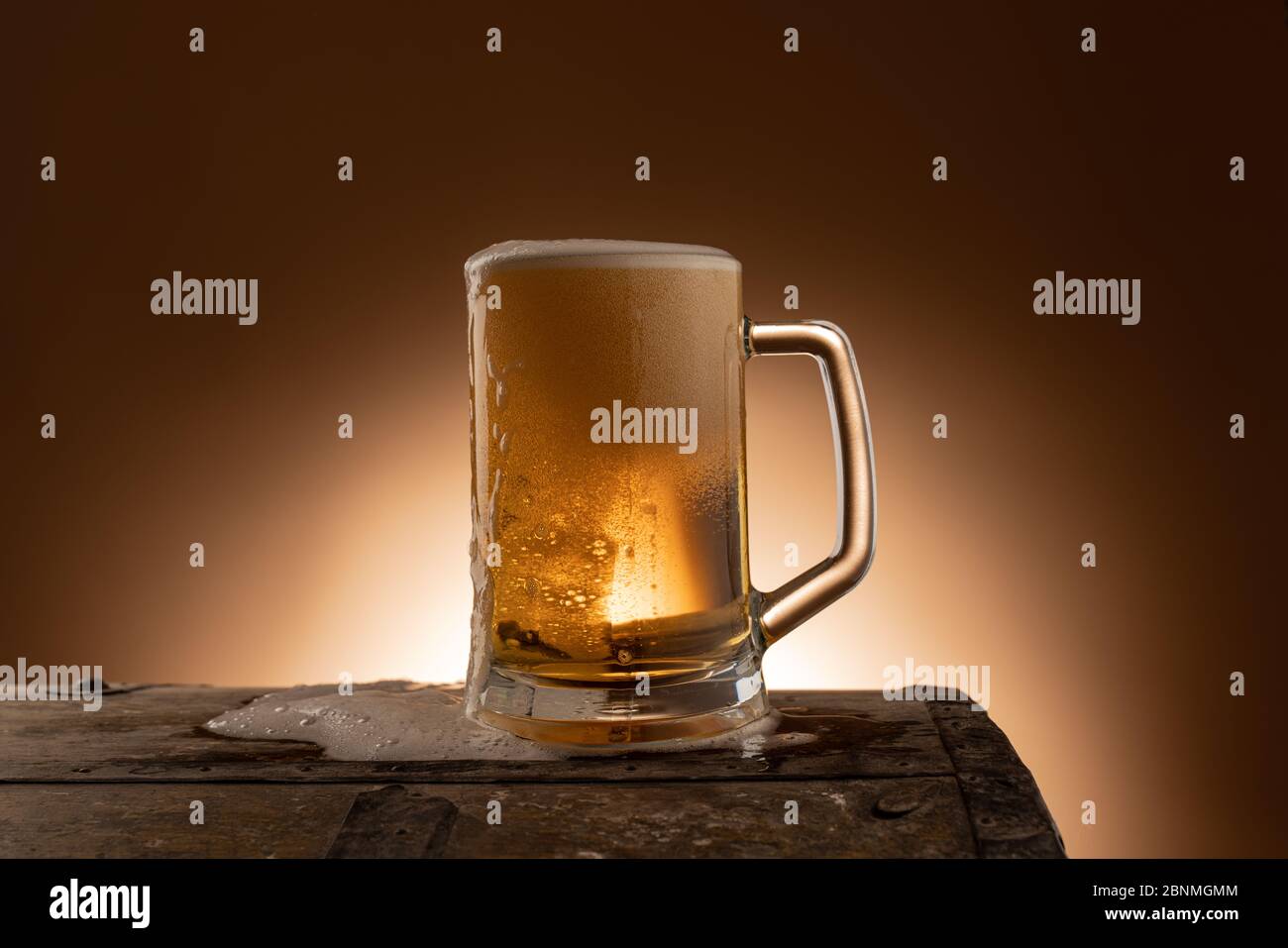 Birra fresca in tazza su un tavolo di legno con schiuma rovesciata, una bella parete arancione scuro come sfondo in un ristorante Foto Stock