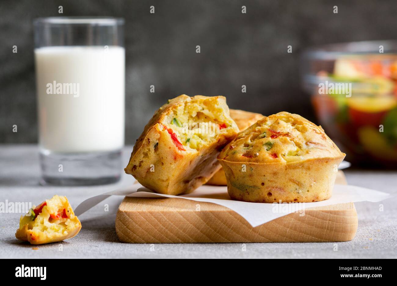 Muffin alle verdure con formaggio su un tagliere. Insalata e latte su sfondo grigio. Cibo vegetariano sano, pasto, cena o spuntino. Primo piano. Foto Stock