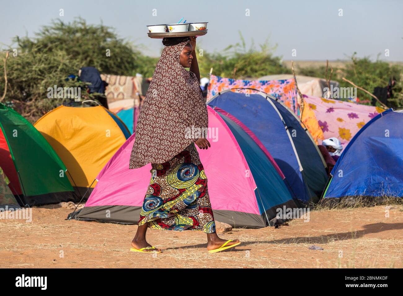 Donna in abiti tradizionali portare il cibo in tenda campo in Sahel zona Foto Stock