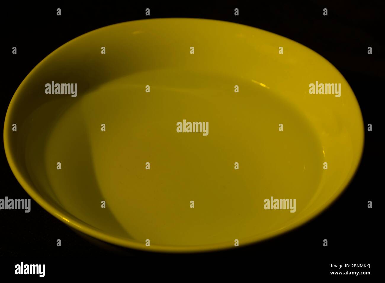 Ciotola bianca piena d'acqua su fondo nero, acqua calma, colore giallo scuro Foto Stock