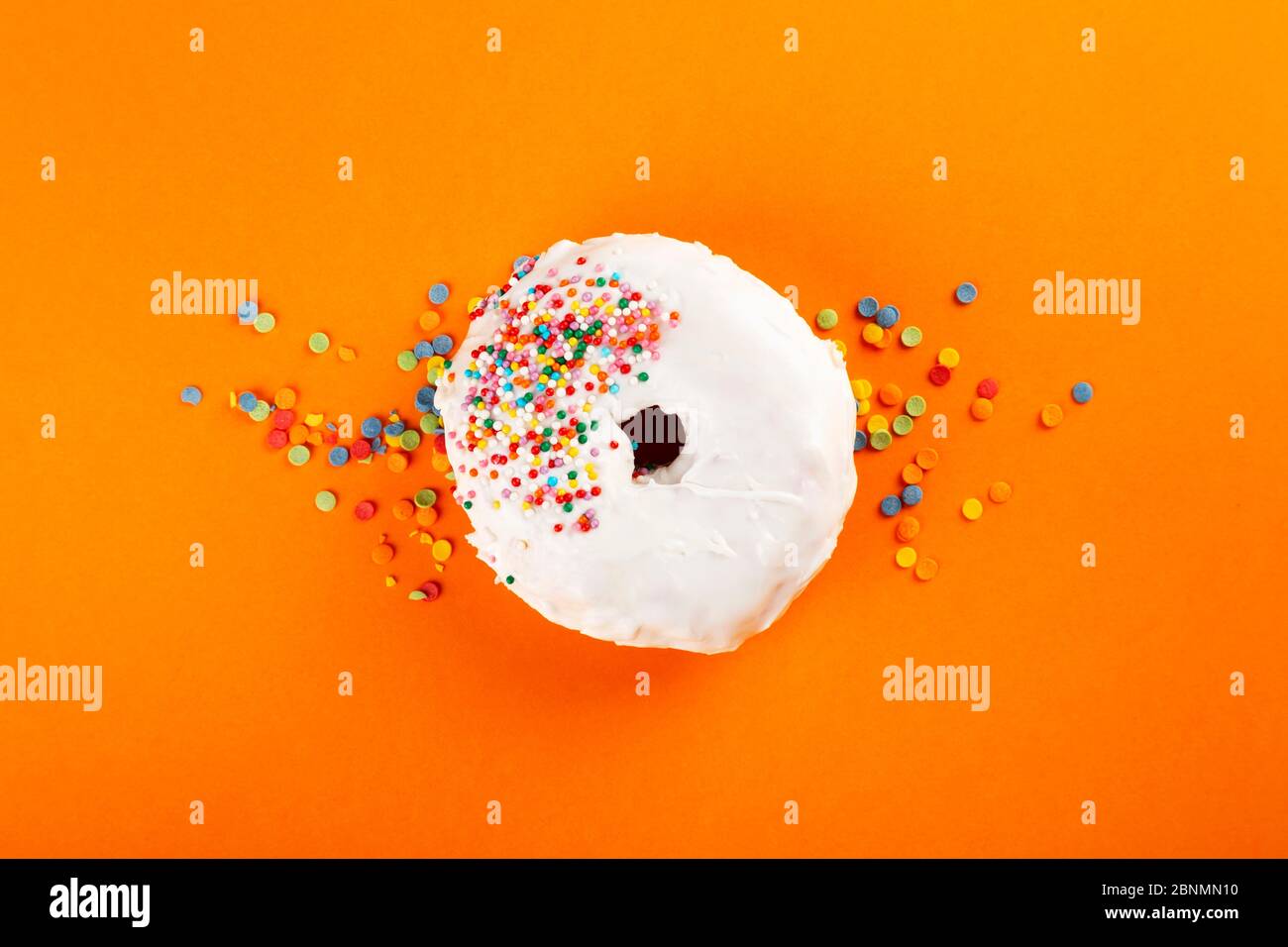 Ciambella con glassa bianca e pasta di zucchero multicolore su fondo arancione. Vista dall'alto Foto Stock