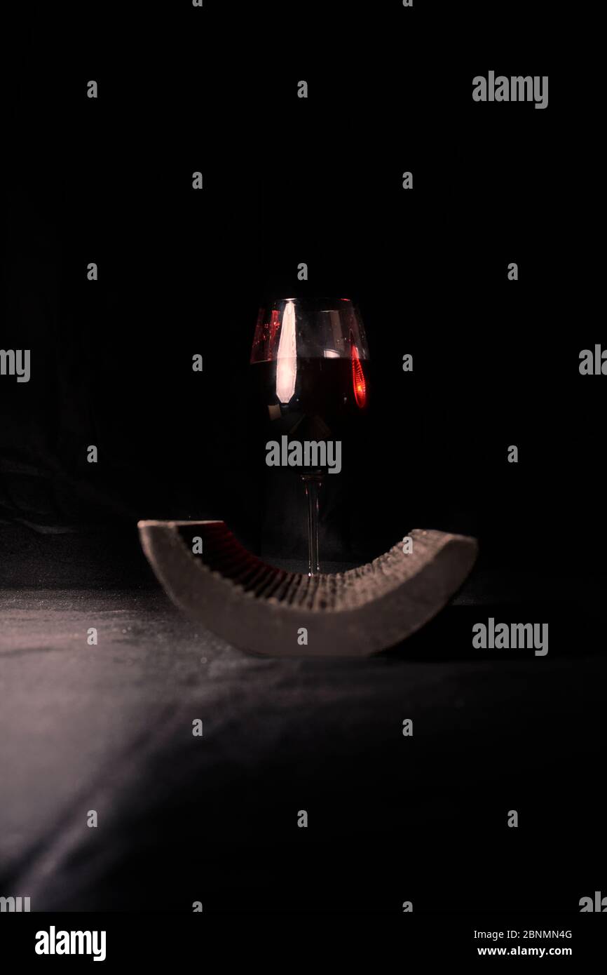 Bicchiere di vino rosso, accanto ad una piastrella, su sfondo nero Foto Stock