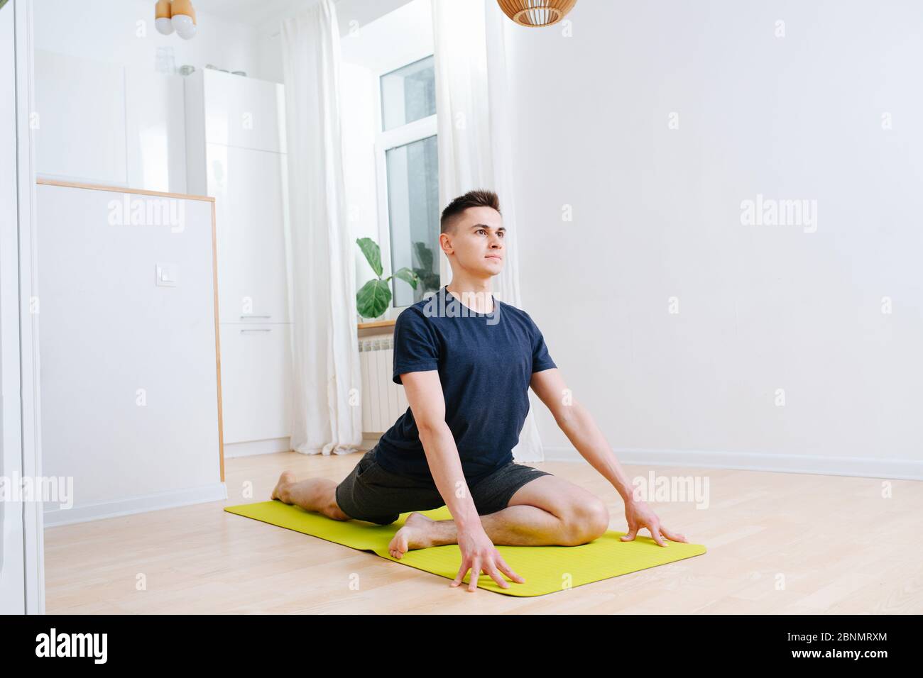 Risolto, deteminato giovane uomo che fa yoga su un tappetino a casa, sollevando la parte superiore del corpo Foto Stock