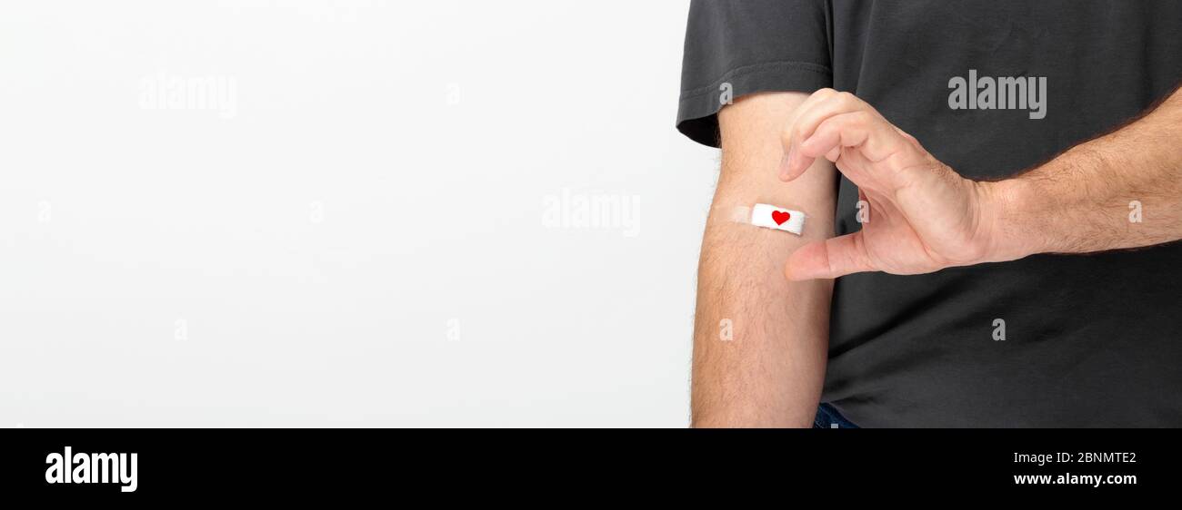 Donazione di sangue. Uomo in grigio T-shirt mano con cerotto con cuore rosso dopo aver dato sangue su sfondo grigio. Mostra mezzo cuore con la mano. Copia Foto Stock