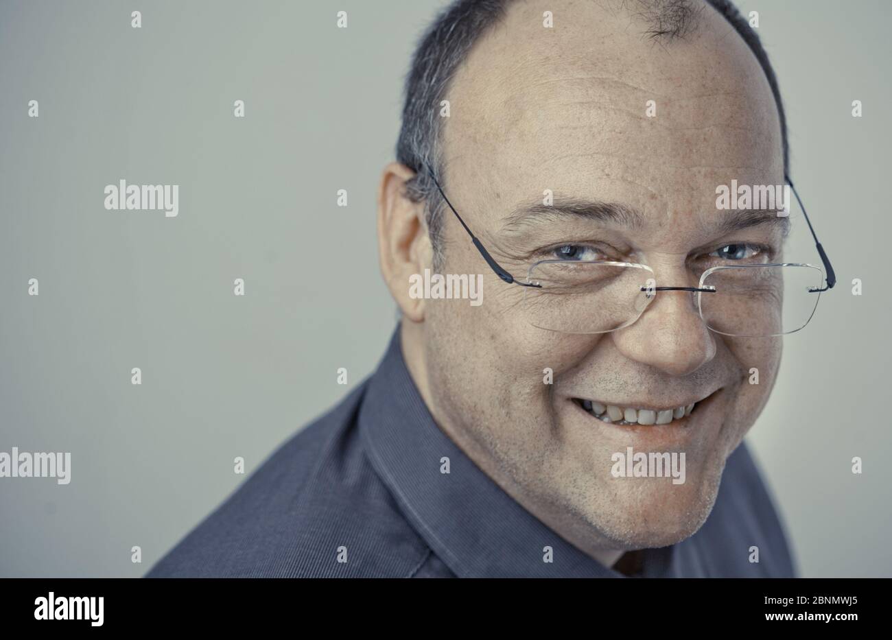 L'uomo anziano con gli occhiali e la testa calva guarda felicemente alla macchina fotografica Foto Stock