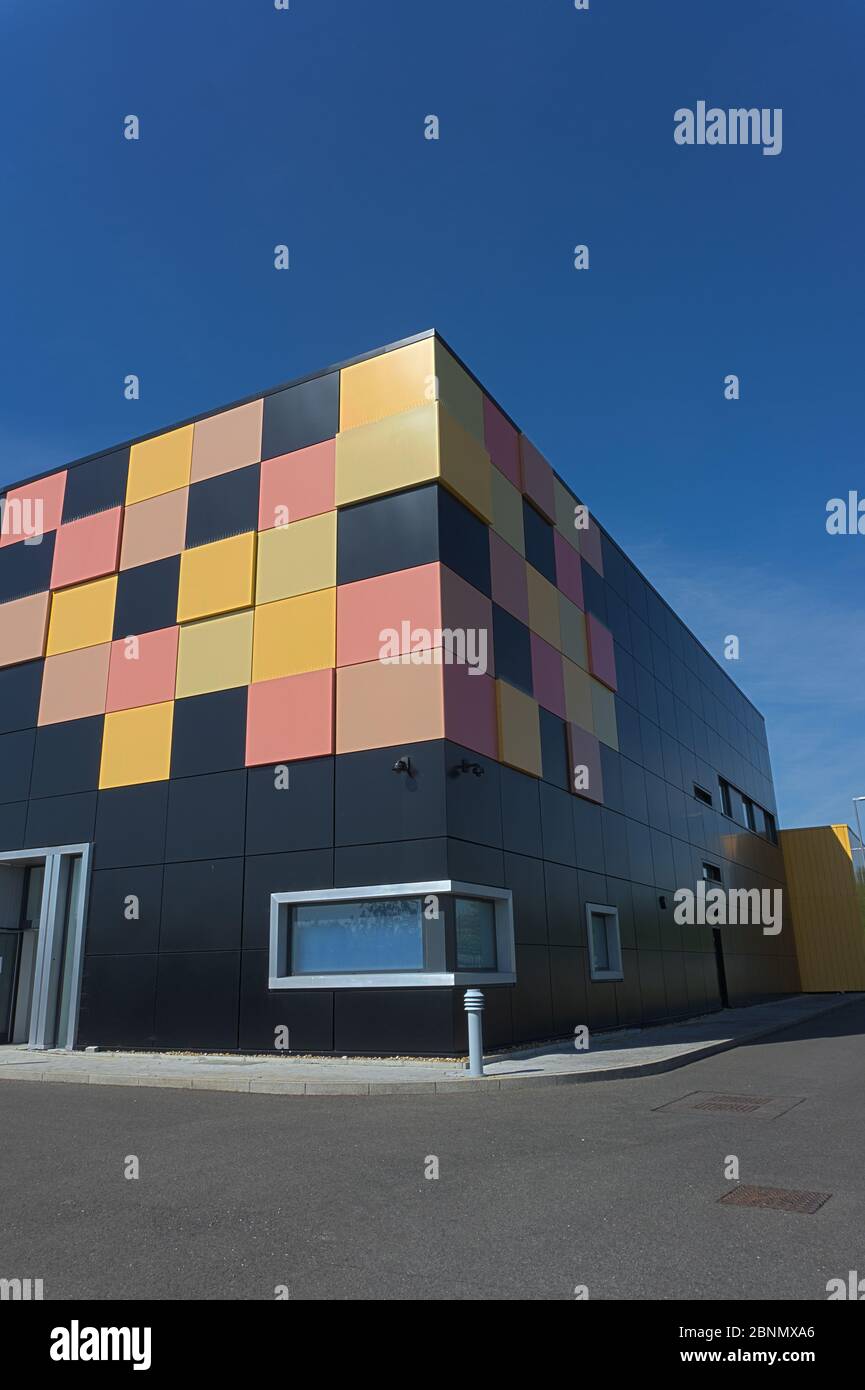 Edificio cubico nero opaco con piastrelle gialle e rosse in un angolo come design grafico dietro le ringhiere di sicurezza in metallo, data center cielo blu intenso Foto Stock