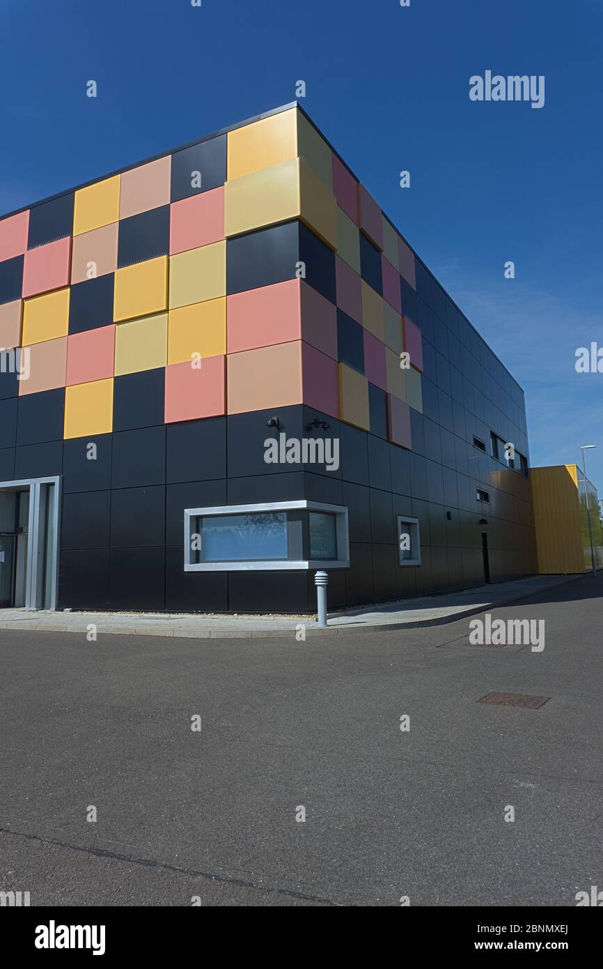 Edificio cubico nero opaco con piastrelle gialle e rosse in un angolo come design grafico dietro le ringhiere di sicurezza in metallo, data center cielo blu intenso Foto Stock