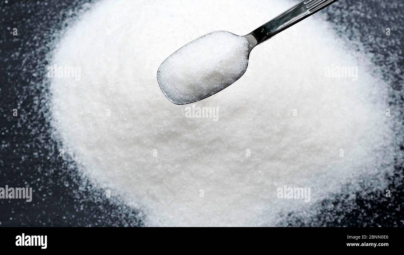 Lo zucchero che cade dal cucchiaio su sfondo nero. Foto Stock