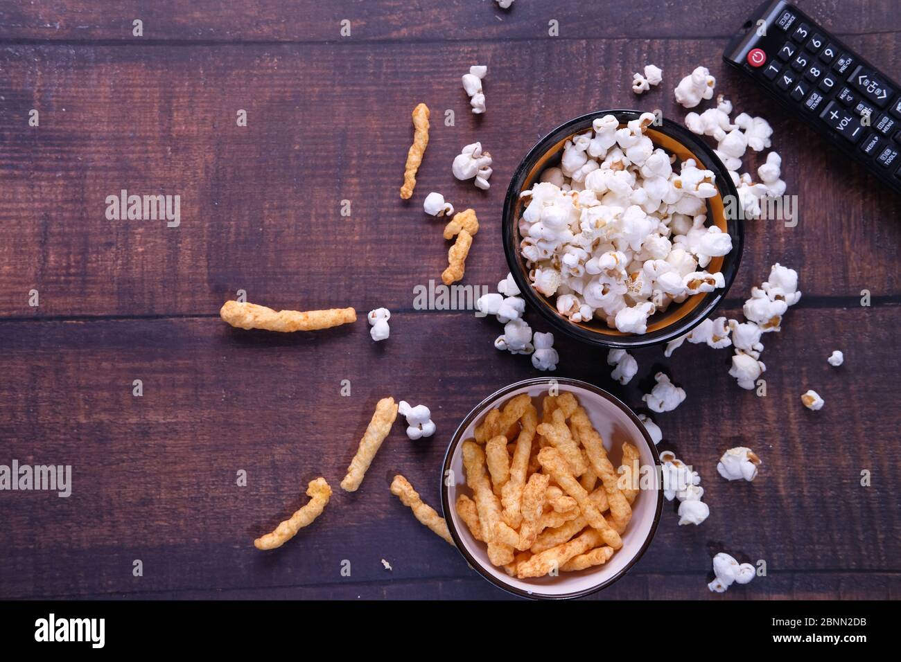 Vista dall'alto di una ciotola di popcorn, patatine e telecomando tv su sfondo di legno Foto Stock