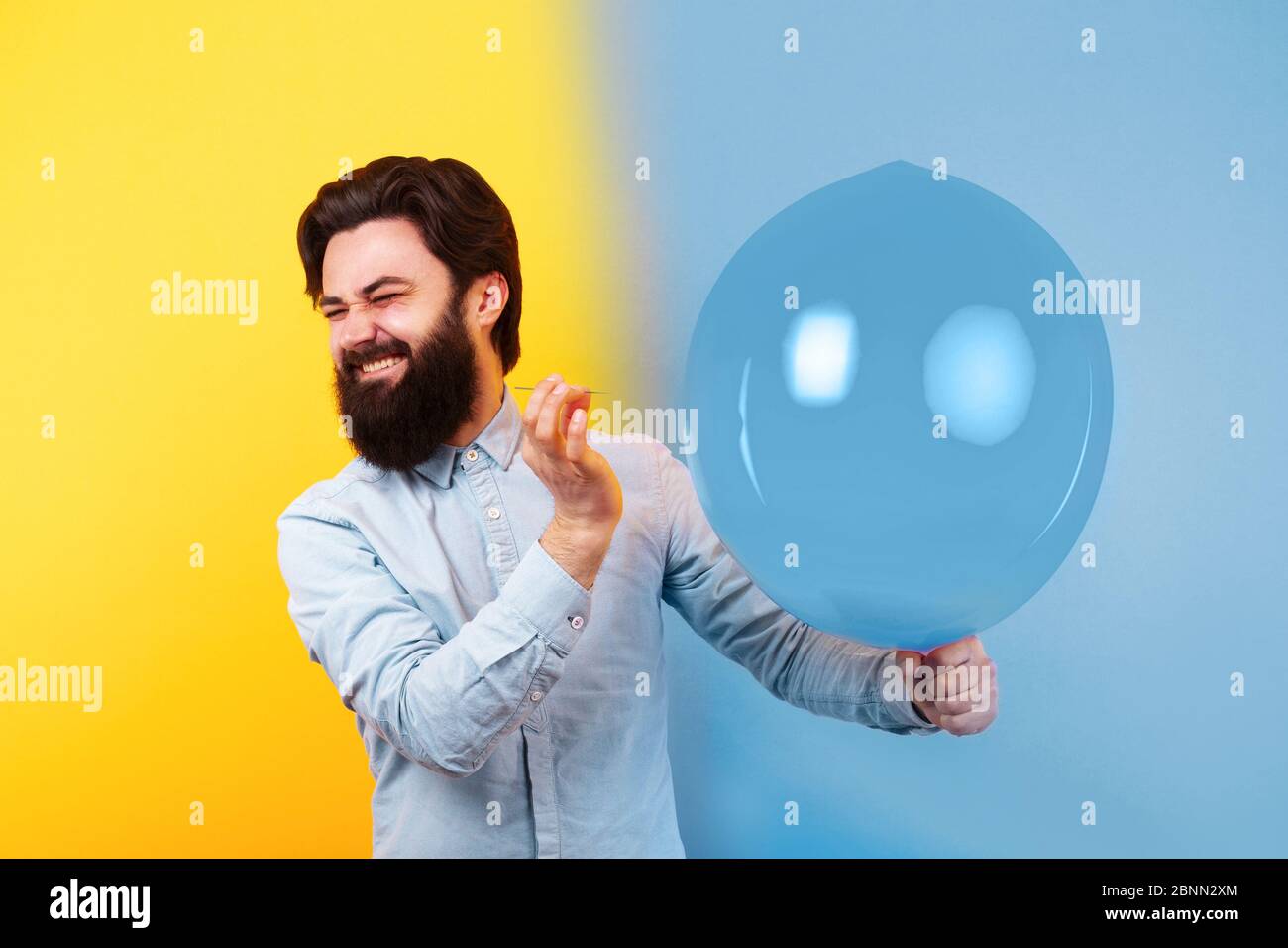 Uomo che tiene l'ago sopra il palloncino giallo dell'aria, un momento prima che scoppiino le bolle, immagine tonica Foto Stock