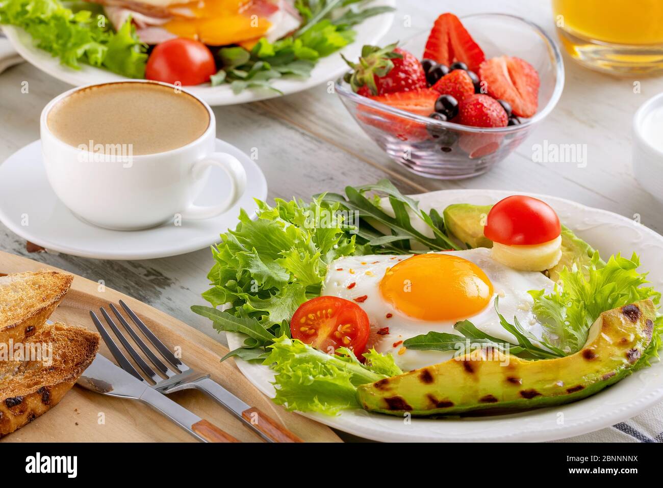Colazione salutare con uova fritte, avocado, pomodoro, toast, caffè e succo d'arancia su sfondo di legno. Concetto di colazione europea o americana. Clos Foto Stock