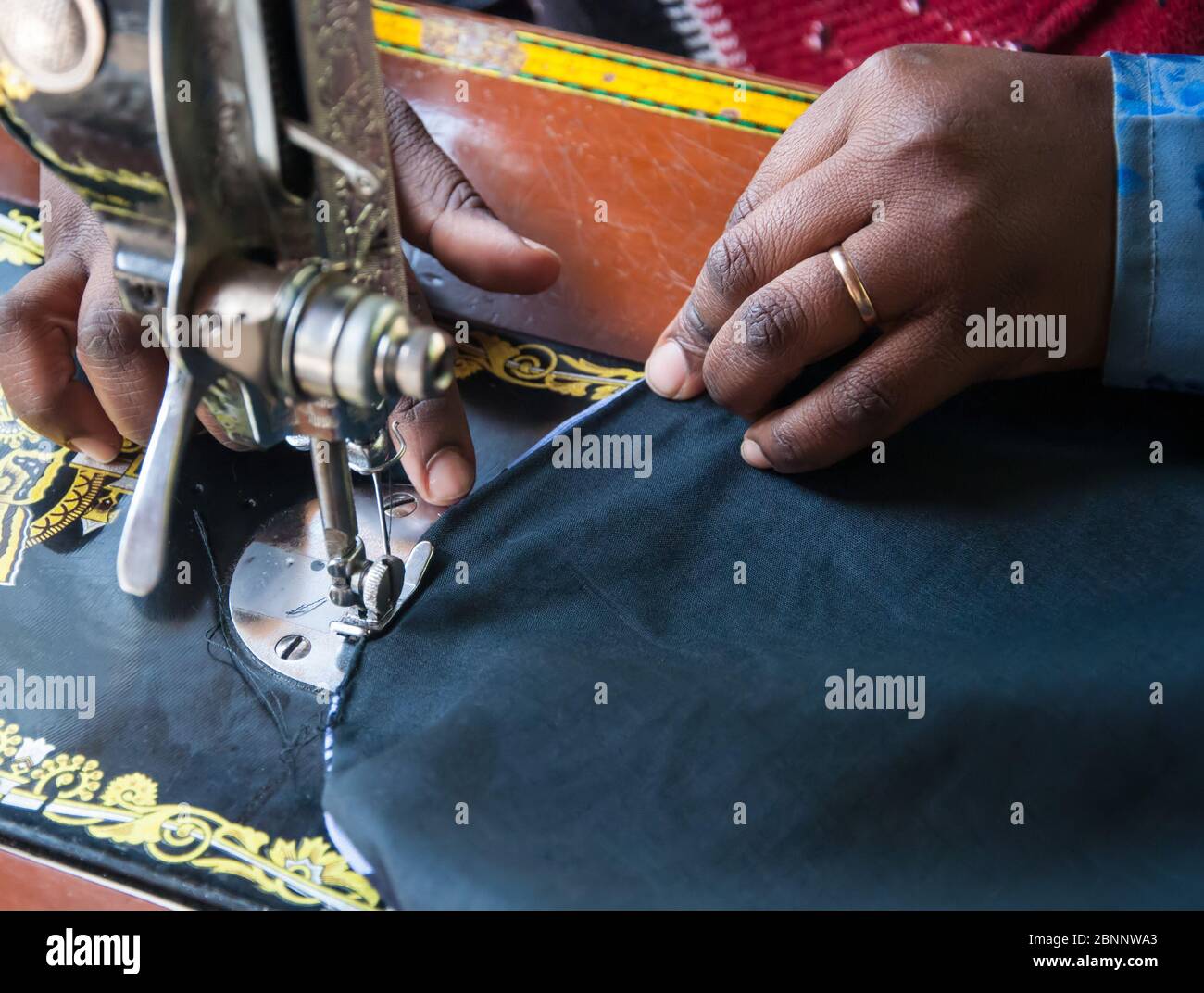 Closeup della mano di donna africana che indossa una banda di nozze, cucire su una macchina da cucire. Foto Stock
