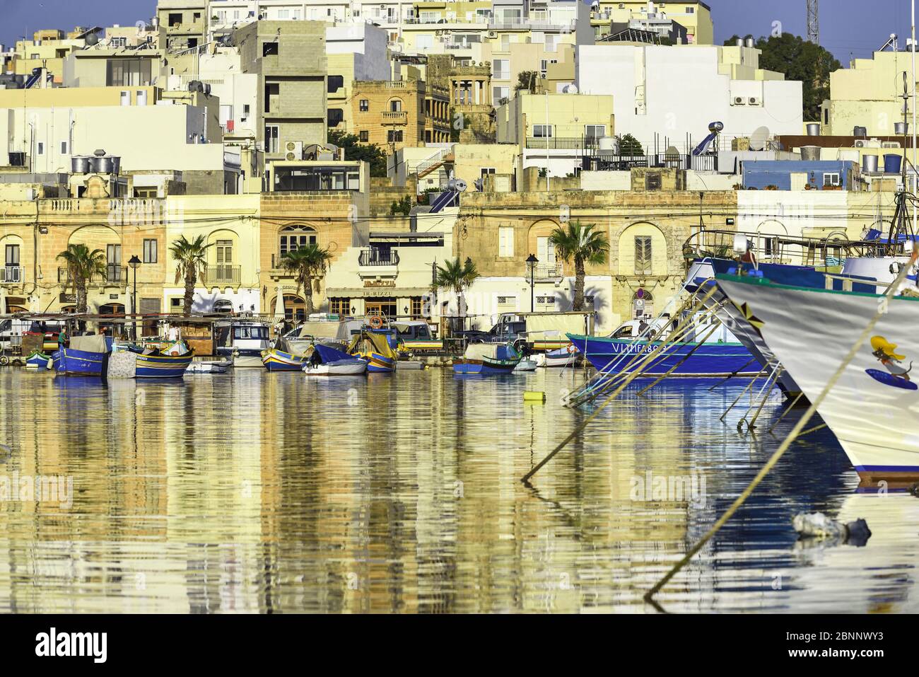 Umore per il tramonto nel porto di Marsaxlokk con le tipiche barche da pesca colorate, sviluppo urbano in background crescente Foto Stock