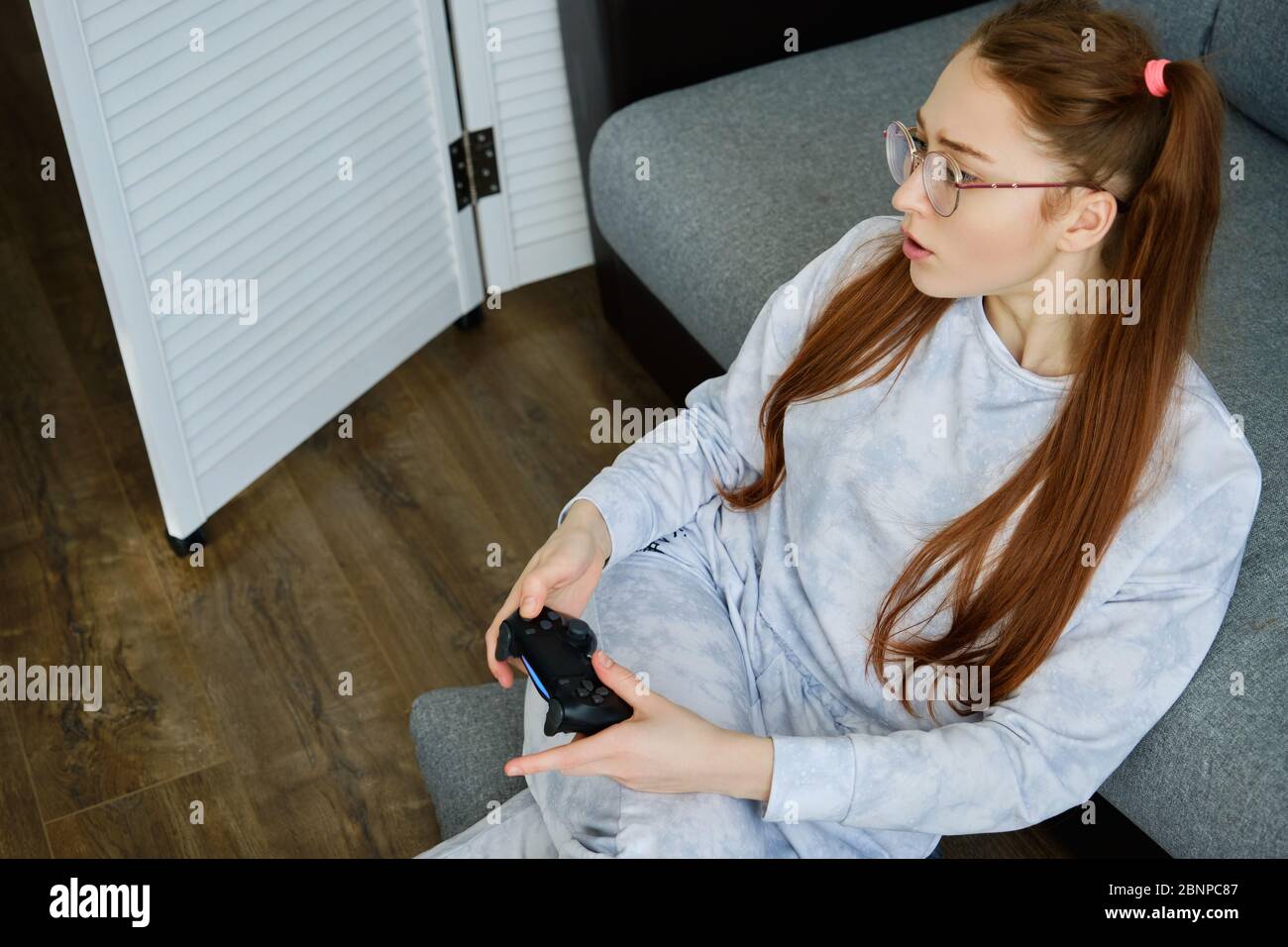 Ragazza rossa in pigiama si siede sul pavimento con un joystick di gioco, la vista dall'alto. Foto Stock