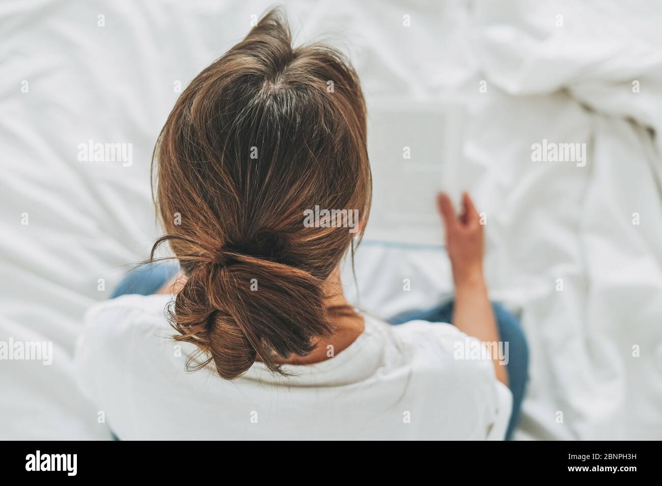 Donna brunetta leggere libro sul letto con biancheria bianca, vista dall'alto Foto Stock