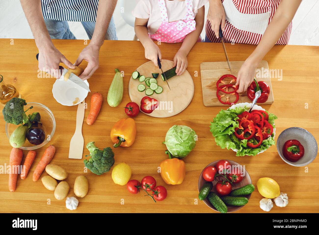 La famiglia cuoce verdure fresche sul tavolo in cucina. Mani di padre e figlia madre con un coltello stanno preparando un'insalata di vitamina. Nessuna faccia. T Foto Stock
