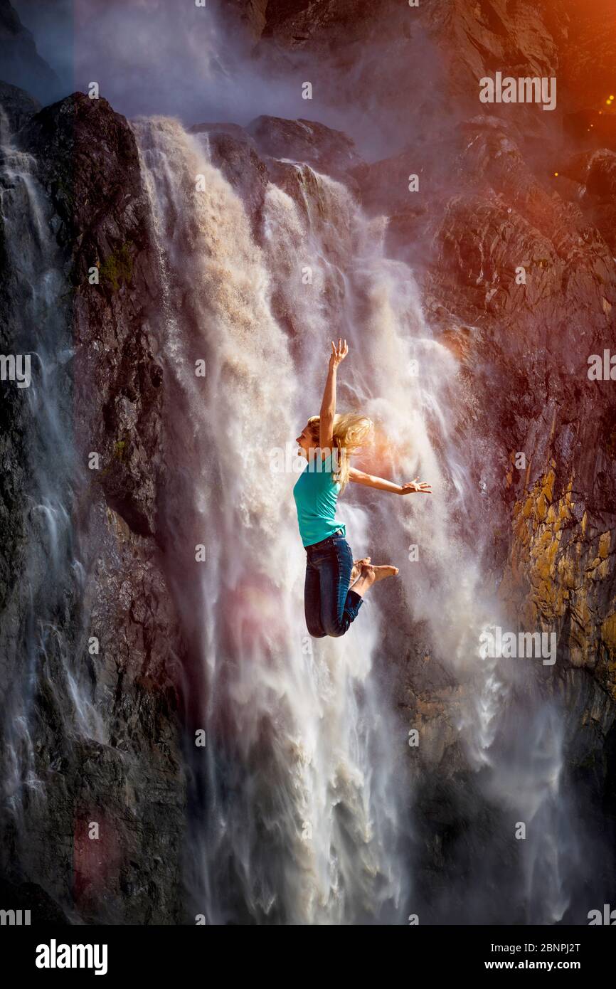 Una donna salta di fronte a una cascata Foto Stock