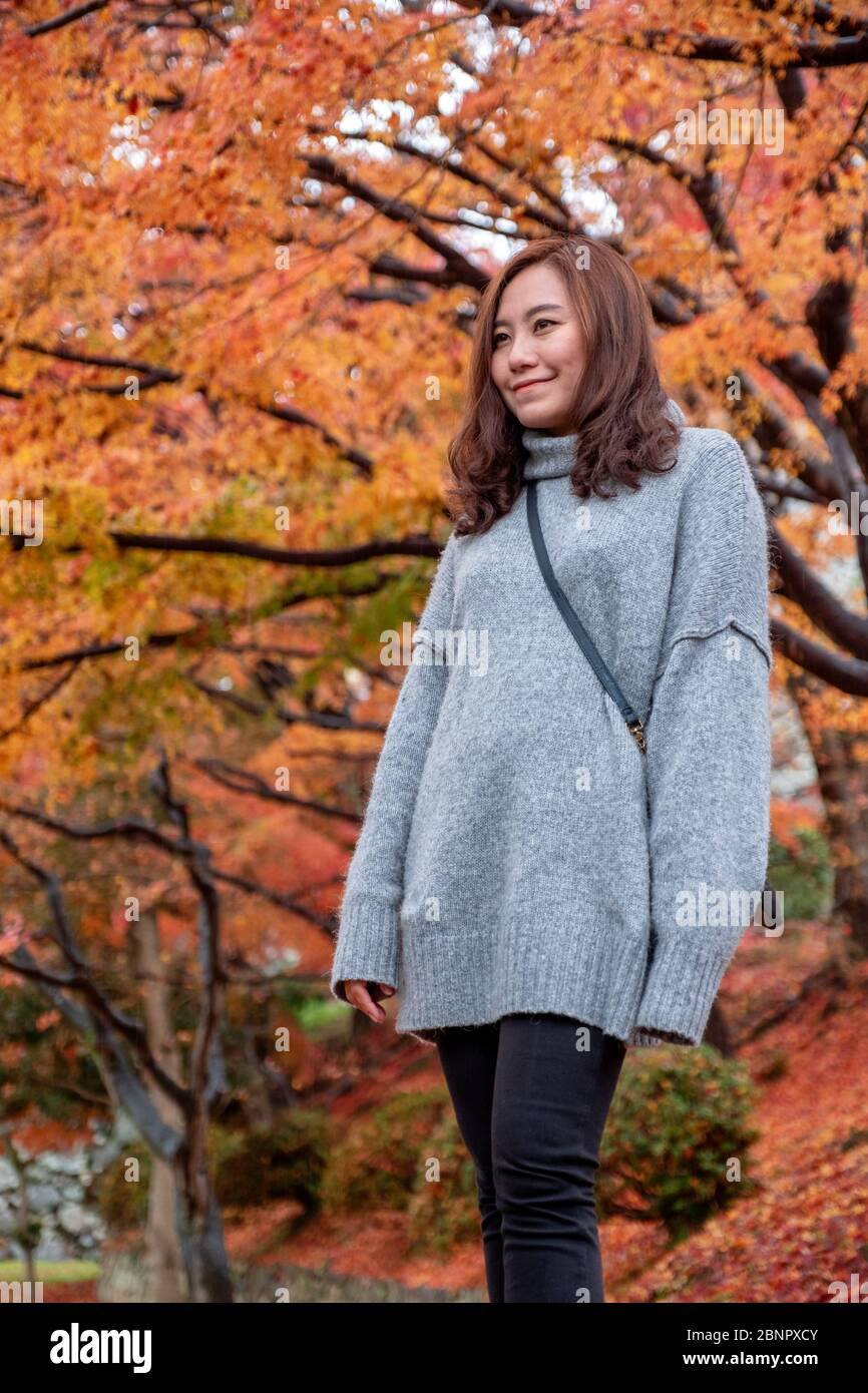 Una bella donna asiatica si è divertita a stare in giardino con foglie di alberi rosso e arancio in background autunno Foto Stock