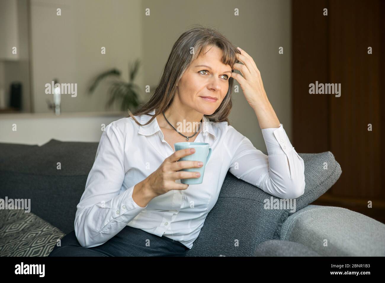 Donna di mezza età in contesti formali ware tenendo una tazza di caffè nel suo appartamento di città Foto Stock