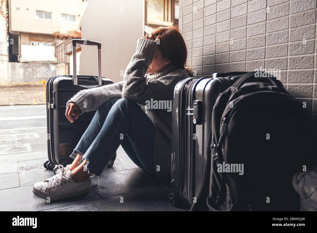 Una donna seduta con sensazione di tristezza e smarrimento durante il viaggio con un sacco di bagagli sul pavimento Foto Stock