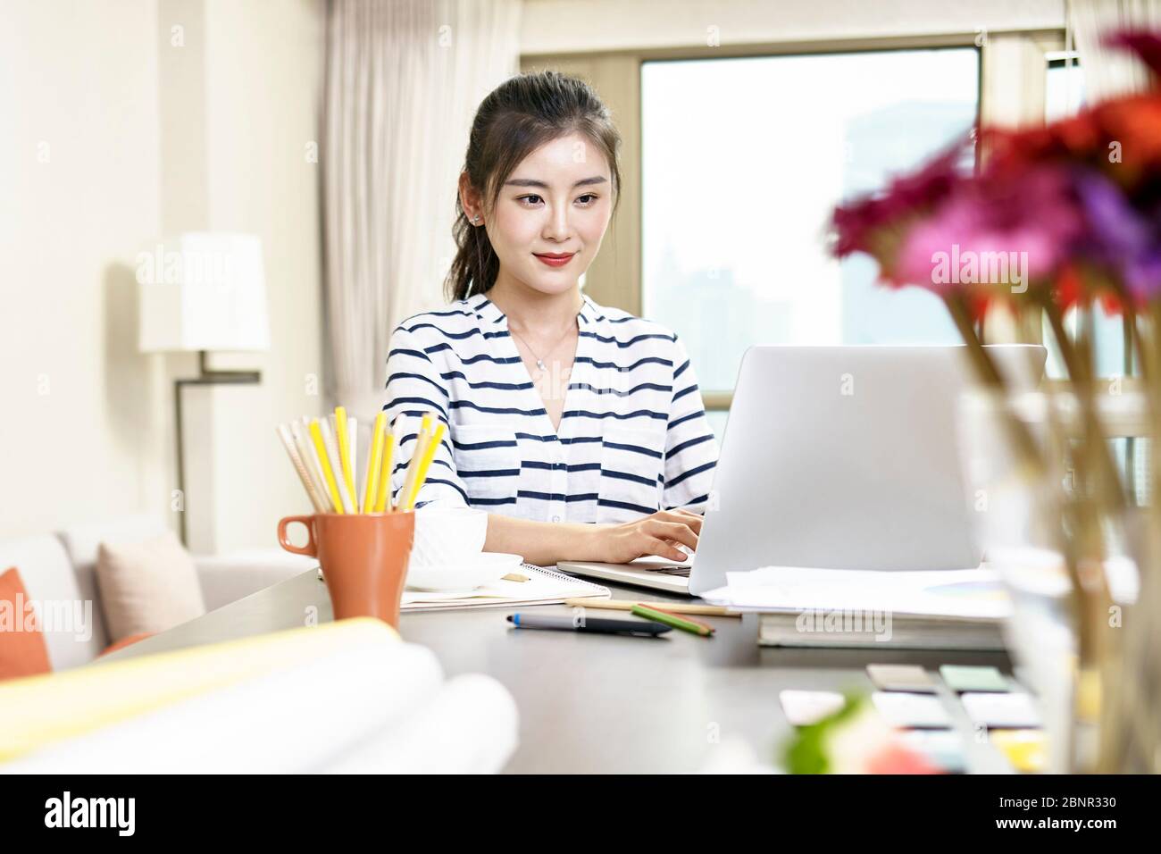 giovane donna asiatica che lavora a casa utilizzando un computer portatile Foto Stock