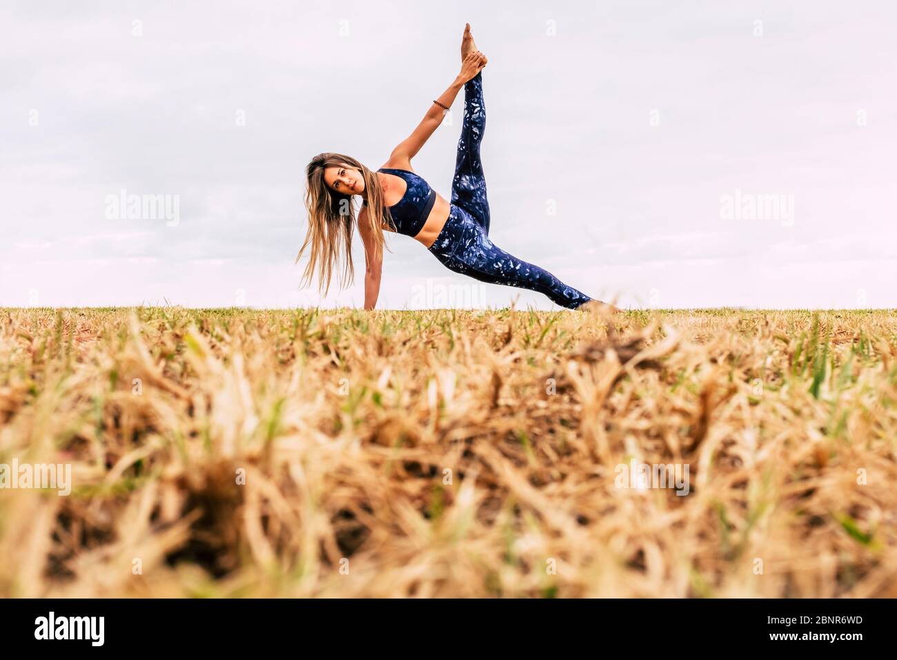 Giovane bella donna caucasica facendo equilibrato pilates posizione di fitness nel prato all'aperto natura - sano stile di vita e attività sportiva concetto di persone - cielo bianco sfondo Foto Stock