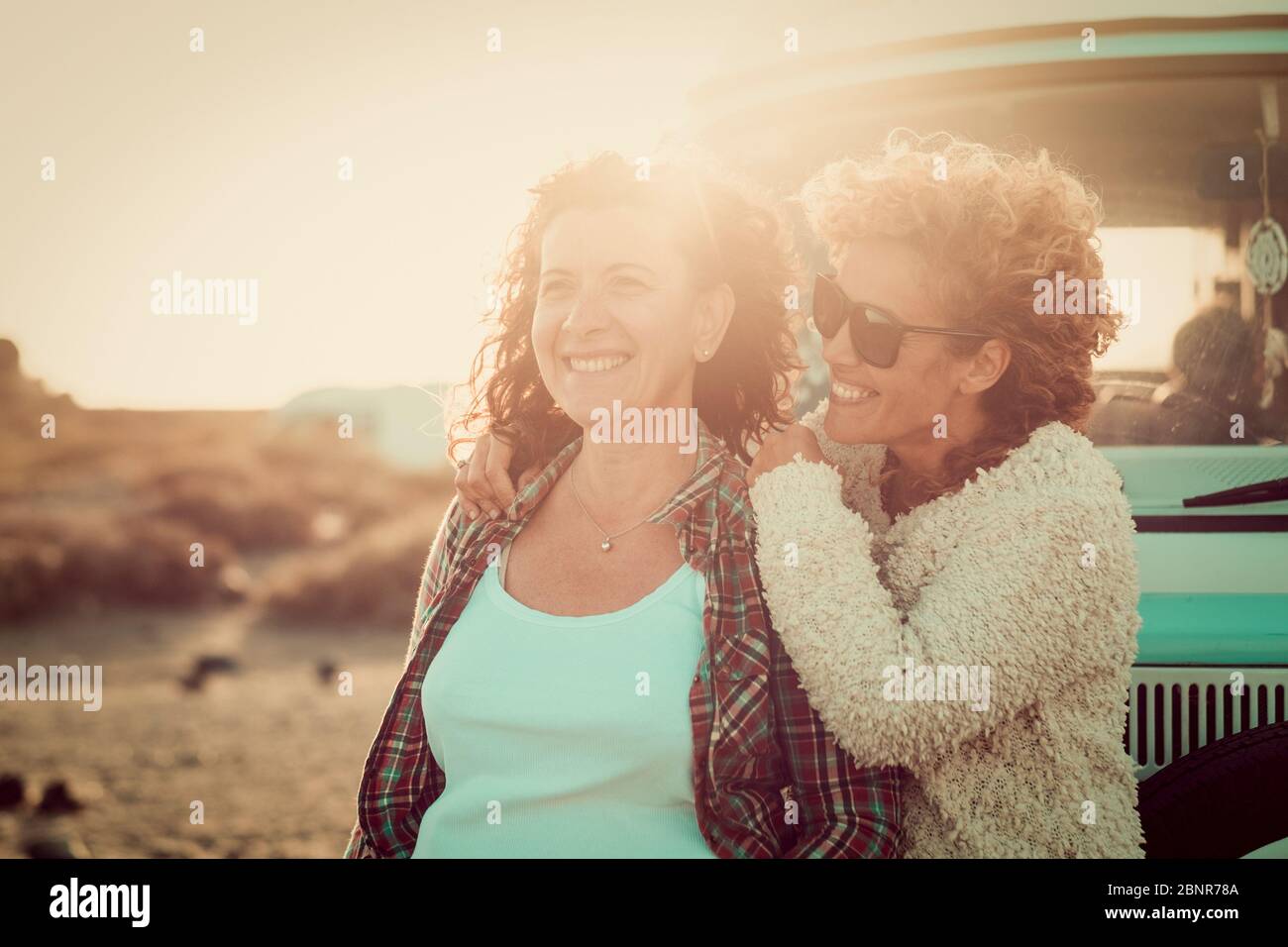 Coppia di allegre donne felici amici adulti godersi insieme l'attività di svago all'aperto divertendosi e sorridendo - van vintage blu in background per concetto di viaggio - retroilluminazione del tramonto Foto Stock