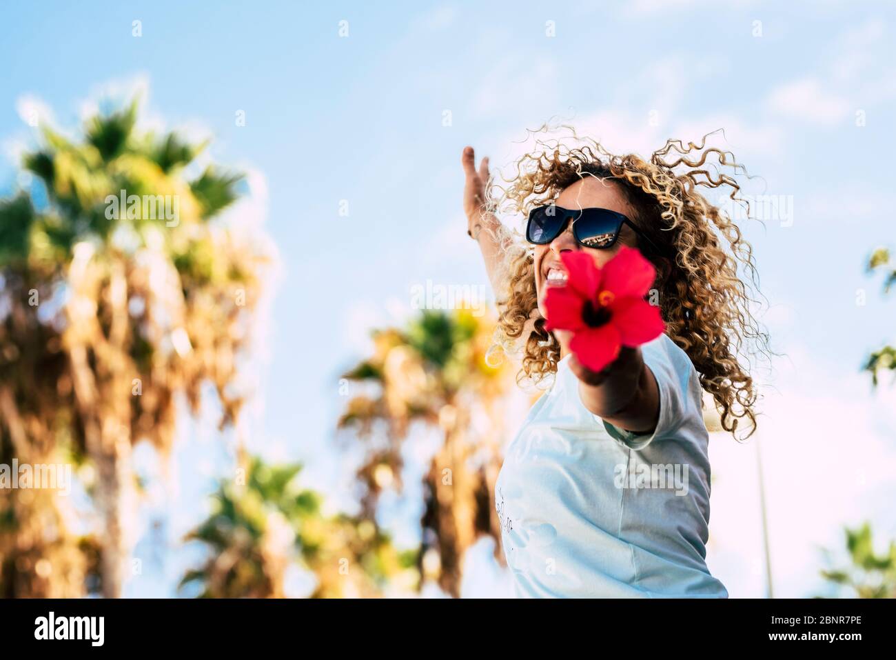 Felicità e fiori rossi - primavera stagione andhapy persone in attività di svago all'aperto - biondo curly bella gente donna adulta saltando e mostrando un grande fiori rossi alla fotocamera Foto Stock