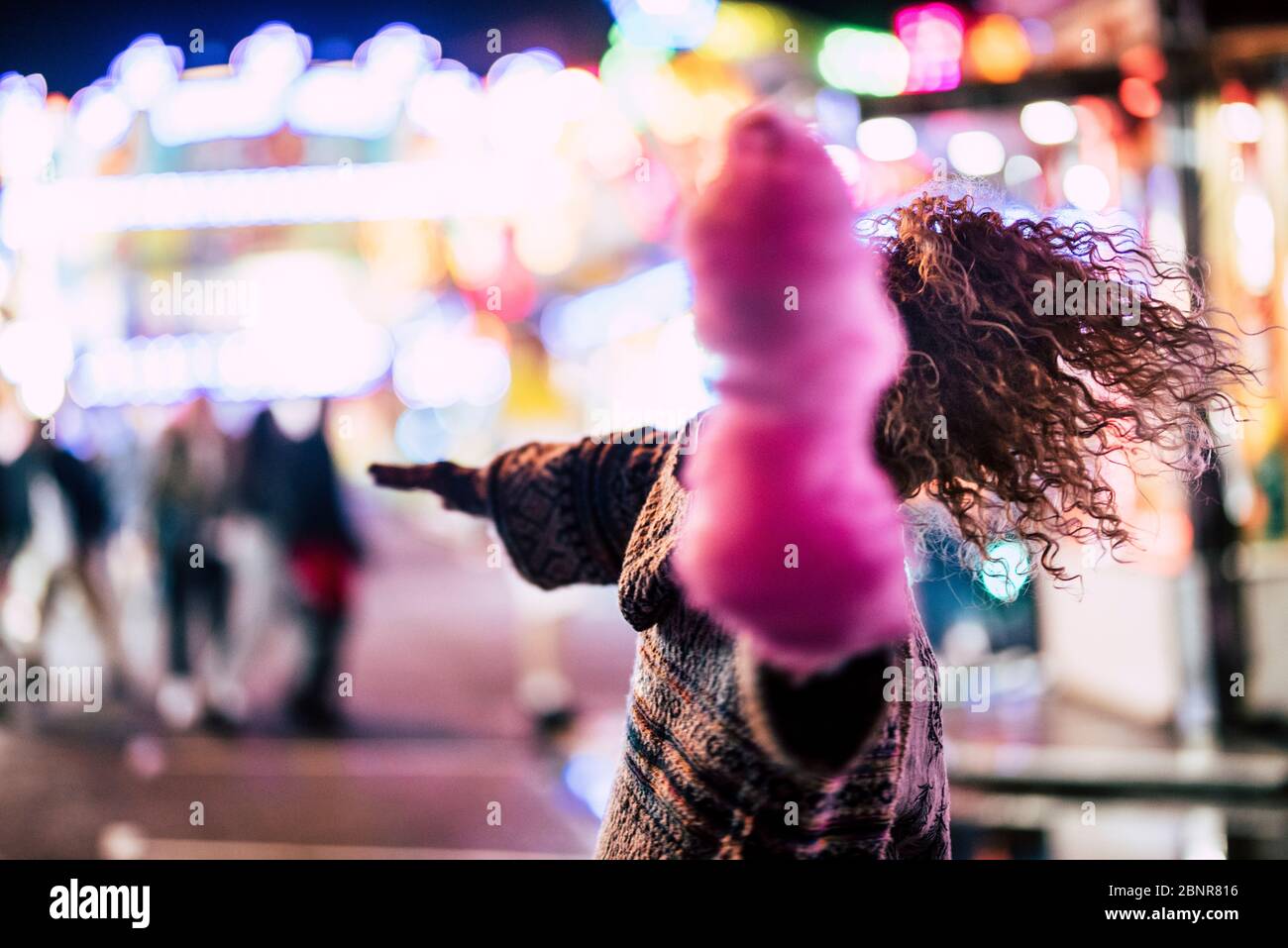 Luna Park e vita notturna con folle signora danza con caramelle di cotone rosa e luci bonek colorate in background Foto Stock