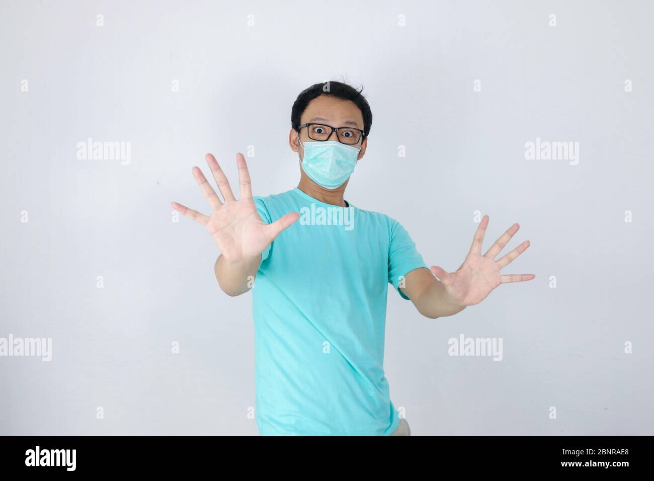 Giovane uomo asiatico indossare maschera igienica è spaventato o panicking con gesturing stop mano. Paura di infezione da coronavirus o malattie respiratorie come f Foto Stock