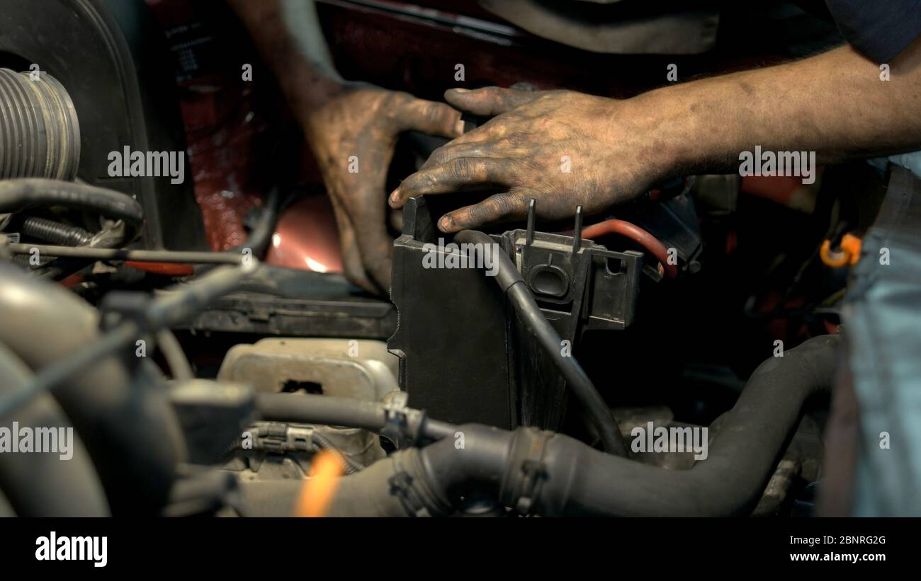 Meccanico con mani sporche disinstallando e riparando i dettagli del motore dell'auto. Foto Stock