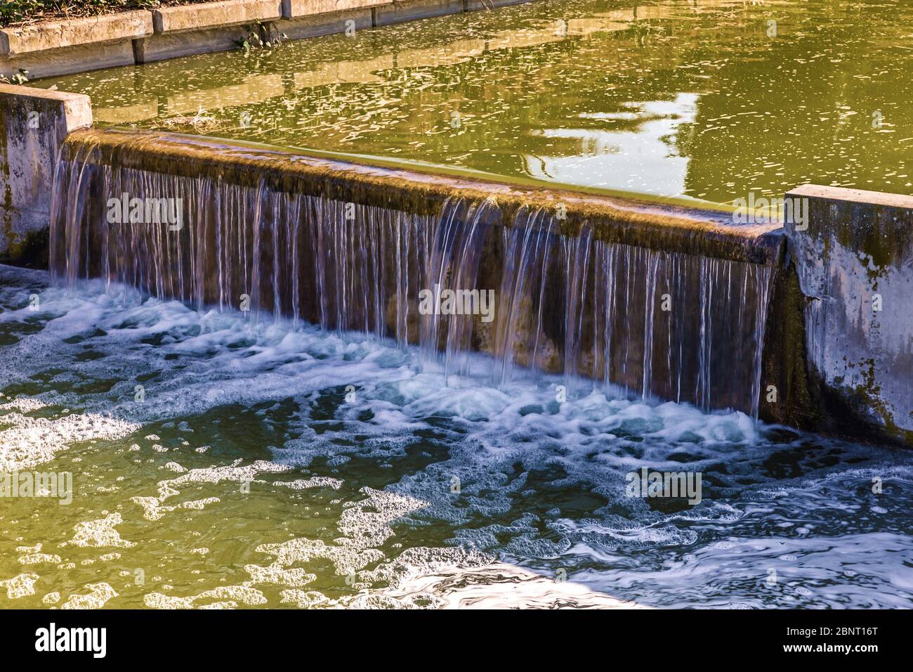 l'acqua che cade attraverso una diga ornamentale in un fiume artificiale nel parco pubblico Foto Stock