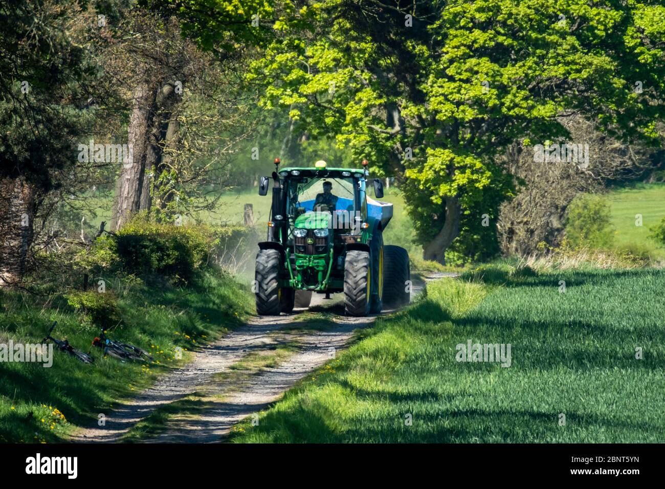 Trattore che traina un lanciarcalce lungo una pista agricola nella Lothian occidentale, Scozia Foto Stock