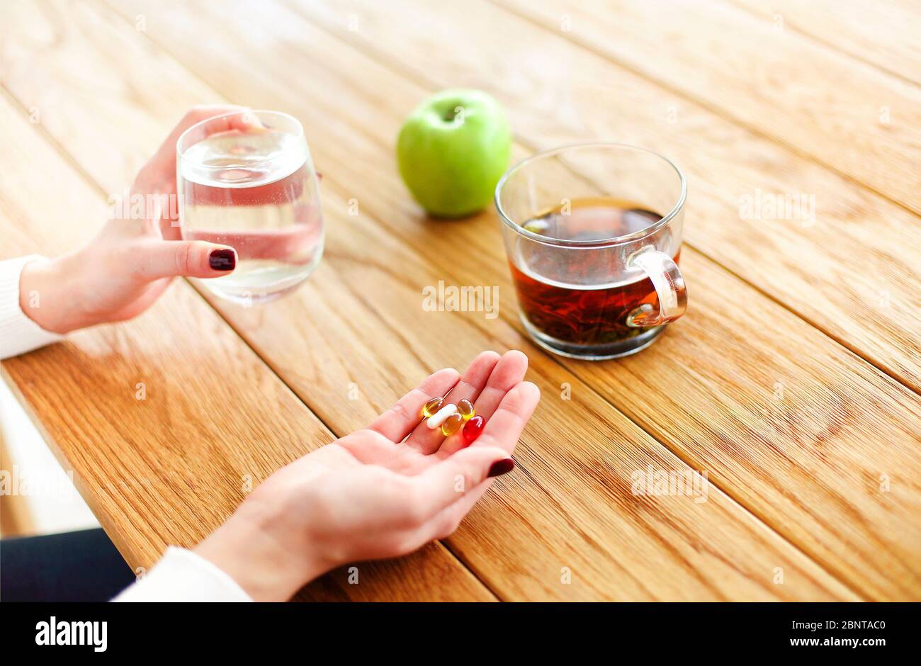 Angolo alto di donna anonima con pillole e tazza d'acqua che strega a tavola con tè e mela durante la malattia Foto Stock