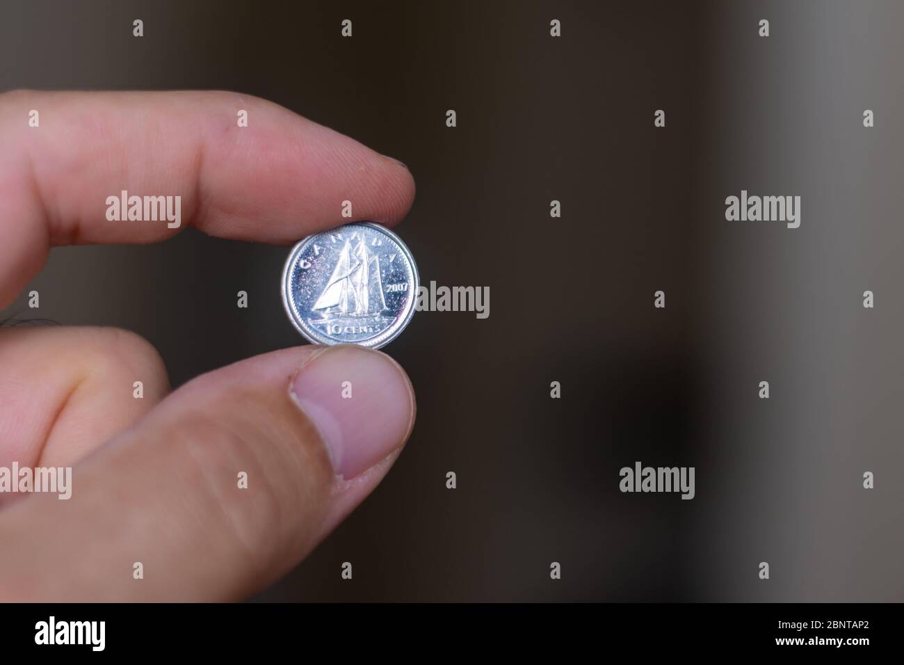 Le persone mano che tiene fuori una moneta di dime o dieci centesimi, la valuta del Canada - su uno sfondo marrone. Cambio di denaro. Foto Stock