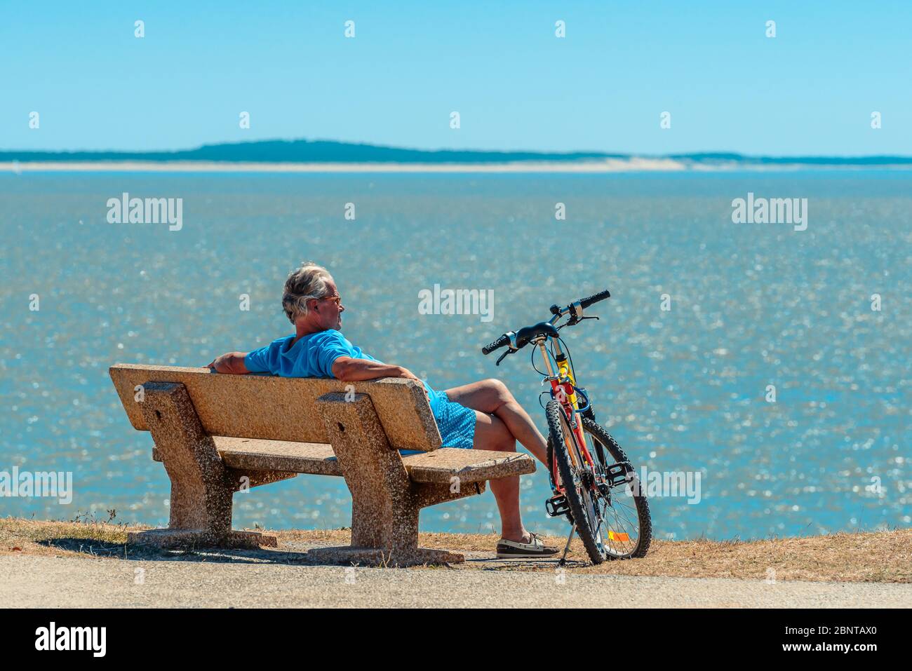 Saint-Palais-sur-Mer, Francia: Un ciclista si siede su una panchina con la sua bicicletta al suo fianco guardando il mare - la baia di Biscay, un golfo dell'Oceano Atlantico. Foto Stock