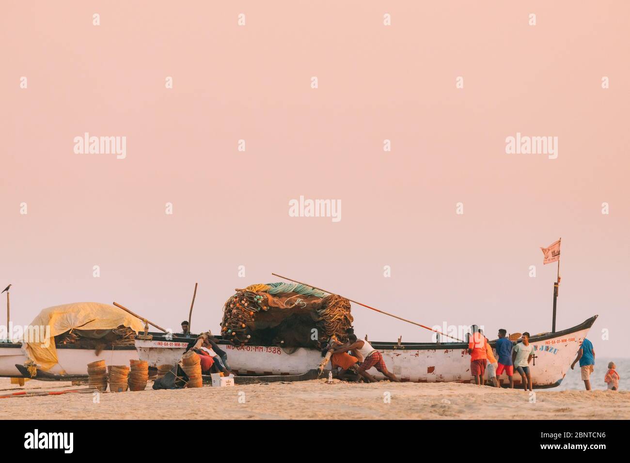 Arossim, Goa, India - 21 febbraio 2020: I pescatori tirano la barca a riva alla fine della giornata lavorativa al tramonto Foto Stock