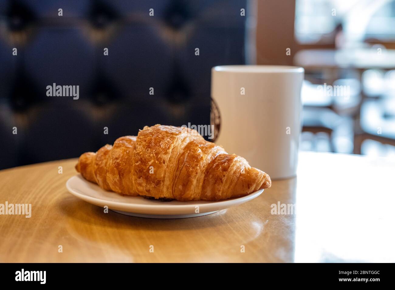 Un pezzo di croissant su un piatto bianco con una tazza di caffè caldo su un tavolo di legno nel caffè Foto Stock