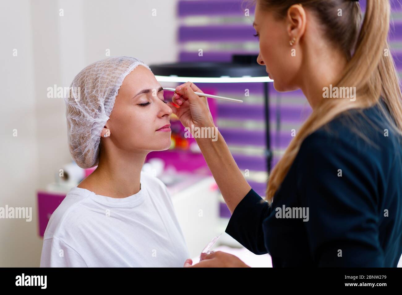 La cosmetologia client cabinet seduto sul divano. Estetista si applica la marcatura sulla sopracciglia. Preparazione per la procedura del sopracciglio permanente del trucco. Free s Foto Stock