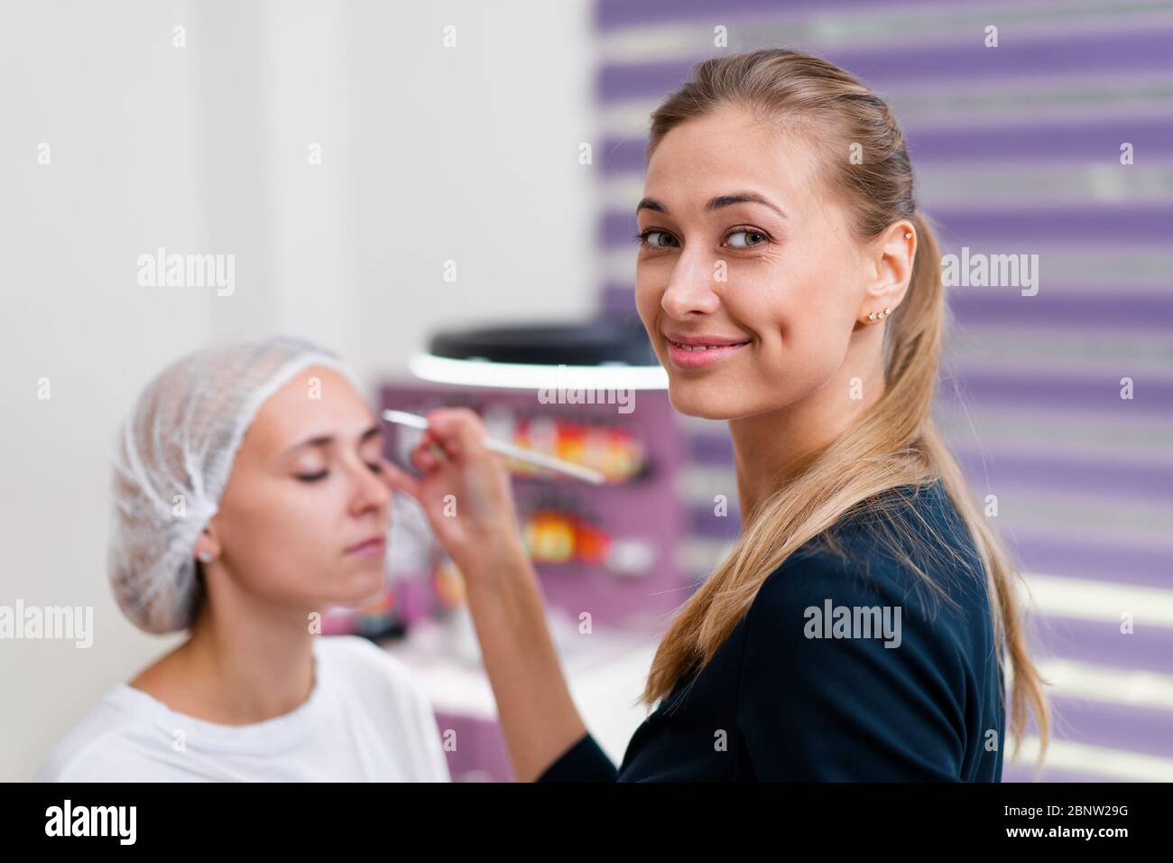 La cosmetologia client cabinet seduto sul divano. Estetista si applica la marcatura sulla sopracciglia. Preparazione per la procedura del sopracciglio permanente del trucco. Free s Foto Stock