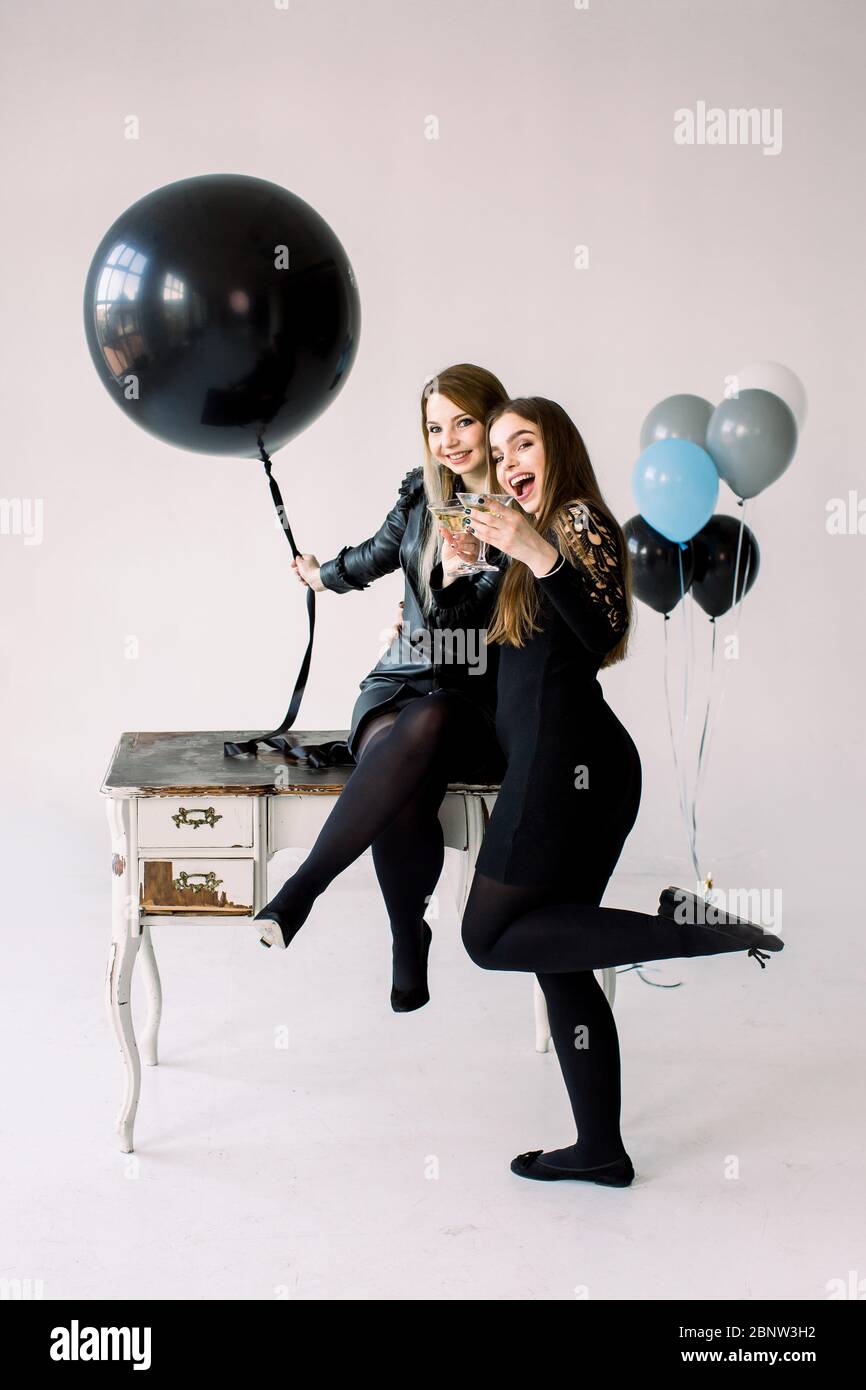 Due giovani donne graziose in abiti neri che tengono i palloncini d'aria insieme, celebrando gallina o compleanno partystanding vicino al tavolo bianco d'annata con Foto Stock