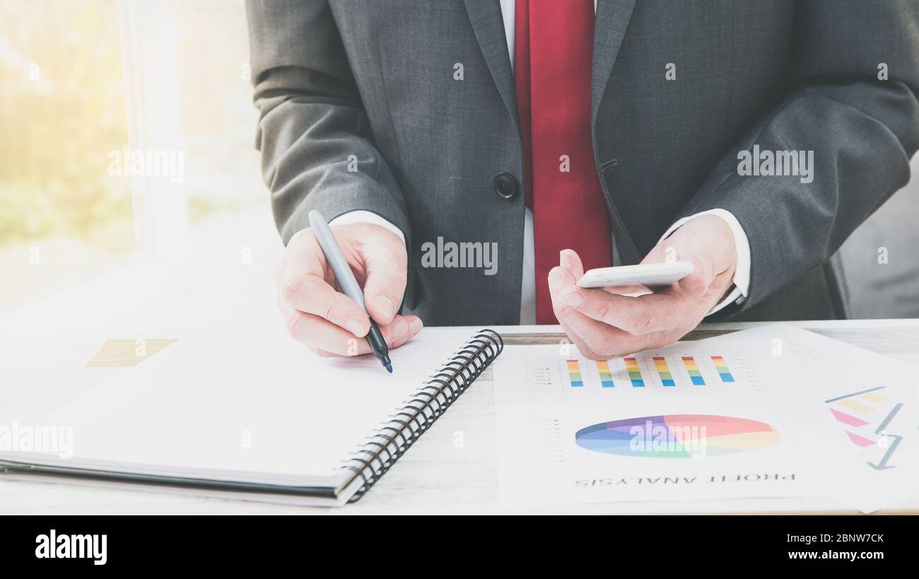 Una sezione centrale di un uomo d'affari alla sua scrivania che analizza e calcola i costi aziendali e la contabilità con i profitti dell'azienda con lo spazio di copia Foto Stock