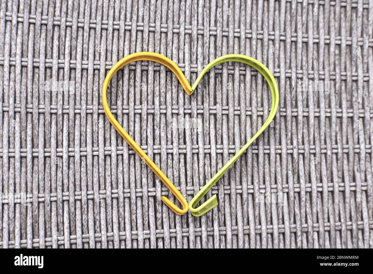 Ganci metallici gialli e verdi che formano insieme una classica forma a cuore su mobili da esterno in rattan. Foto Stock