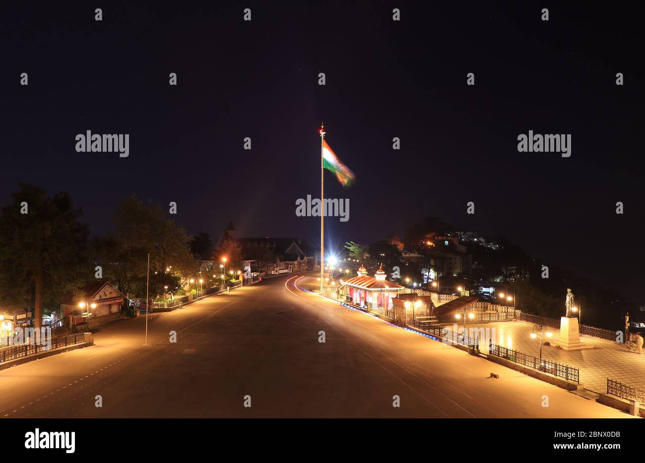 Splendido paesaggio sereno della Mall Road di Shimla di notte. La bandiera indiana si batte in modo glorioso nel vento, mentre un cane si siede pacificamente sul ro Foto Stock